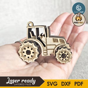 May include: A laser-cut wooden tractor with detailed wheels, cabin, and exhaust. The tractor is light brown and has a small loop at the top. The image includes the text "Laser ready" and "SVG DXF PDF".