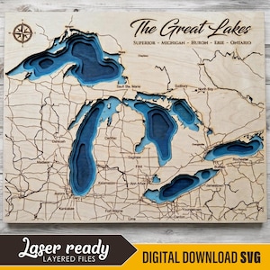 May include: A layered wooden bathymetric map of The Great Lakes, featuring Superior, Michigan, Huron, Erie, and Ontario. The map displays blue-toned water depths, engraved land borders, city names, and a compass rose in the top left corner.