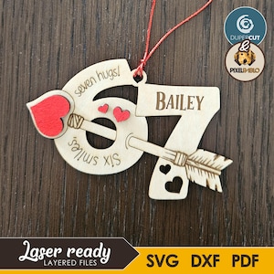 May include: Wooden ornament with the name "Bailey" and the number "67" with an arrow through it. The ornament has the words "seven hugs!" and "six smiles" on it. The ornament has a red string for hanging.