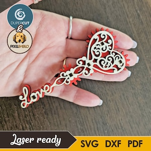 May include: A laser-cut wooden heart-shaped ornament with the word "Love" and intricate scrollwork. The heart is red with a cream-colored overlay, and the design includes decorative elements. The text "Laser ready" is visible.