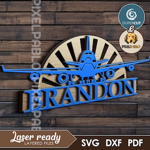 Op de afbeelding: Blauwe vliegtuigsilhouet met een zonsopgangontwerp erachter. De naam "BRANDON" staat in blauwe letters onder het vliegtuig. Het ontwerp is lasergesneden en klaar om in elkaar te zetten.
