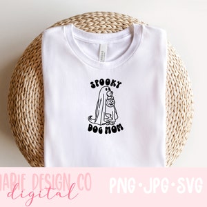 Op de afbeelding: Wit T-shirt met een zwart-witte afbeelding van een hond die verkleed is als een geest en een pompoen vasthoudt. De tekst "Spooky Dog Mom" staat onder de afbeelding.