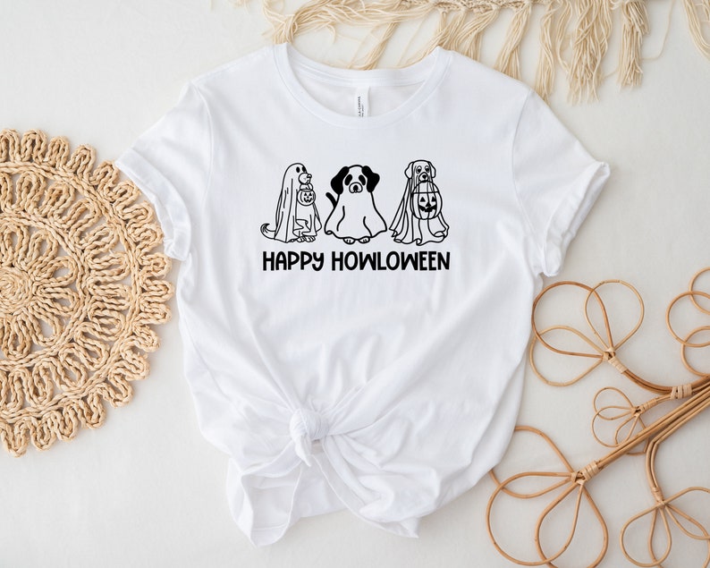 K&ouml;nnte beinhalten: Wei&szlig;es T-Shirt mit einer schwarz-wei&szlig;en Illustration von drei Hunden, die als Geister f&uuml;r Halloween verkleidet sind. Der Text "Happy Howloween" ist unter der Illustration gedruckt.