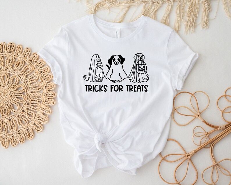 K&ouml;nnte beinhalten: Wei&szlig;es T-Shirt mit einer schwarz-wei&szlig;en Grafik von drei Hunden, die als Geister f&uuml;r Halloween verkleidet sind. Der Text "TRICKS FOR TREATS" ist unter der Grafik gedruckt.