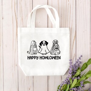 K&ouml;nnte beinhalten: Wei&szlig;e Einkaufstasche mit schwarzen Strichzeichnungen von drei Hunden, die als Geister f&uuml;r Halloween verkleidet sind. Der Text "Happy Howloween" ist unter den Hunden gedruckt.