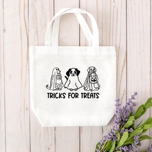 K&ouml;nnte beinhalten: Wei&szlig;e Stofftasche mit schwarzen Strichzeichnungen von drei Hunden, die als Geister verkleidet sind. Der Text "TRICKS FOR TREATS" ist unter den Hunden gedruckt.