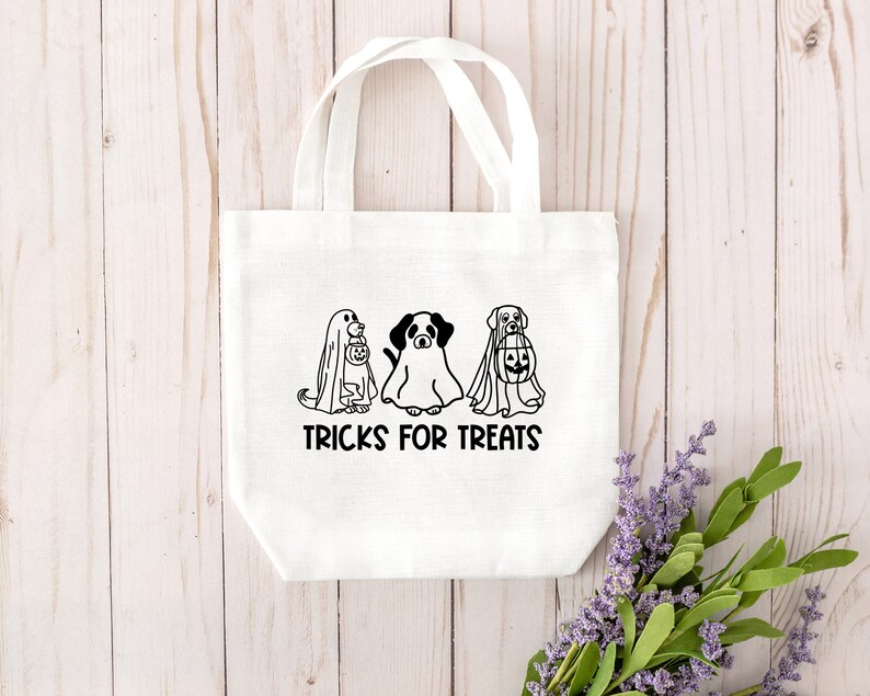 K&ouml;nnte beinhalten: Wei&szlig;e Stofftasche mit schwarzen Strichzeichnungen von drei Hunden, die als Geister verkleidet sind. Der Text "TRICKS FOR TREATS" ist unter den Hunden gedruckt.