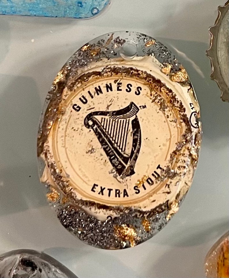 May include: A close-up of a round, white bottle cap with gold and silver glitter. The cap features the Guinness logo, a harp, and the text "GUINNESS EXTRA STOUT".