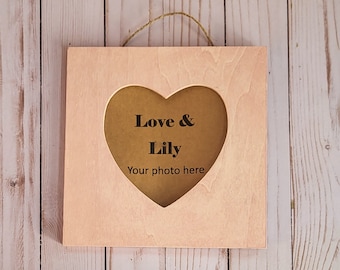 Könnte beinhalten: Ein heller Holzrahmen mit einem herzförmigen Ausschnitt. Der Rahmen trägt den Text "Love & Lily" und "Your photo here".