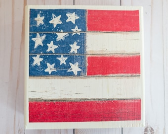 Könnte beinhalten: Ein Holzschild mit einem verwitterten amerikanischen Flaggen-Design. Die Flagge ist in Rot, Weiß und Blau mit weißen Sternen auf einem blauen Feld bemalt.