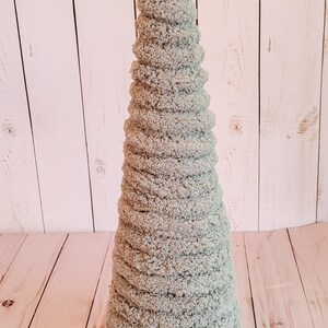K&ouml;nnte beinhalten: Ein hellblauer, kegelf&ouml;rmiger Dekobaum aus weichem, strukturiertem Material. Der Baum ist etwa 30 cm hoch und hat ein spiralf&ouml;rmiges Design. Er steht vor einem hellen Holzhintergrund.