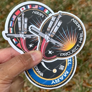 May include: A set of circular stickers with a rocket launch design. The stickers have a black background with the text "PROJECT HAIL MARY" and "MARY" in white. Some stickers include flags and the text "ОХИНА".
