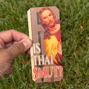 May include: A rectangular bookmark featuring an image of Jesus peeking around a door frame. The text "IS THAT SMUT?" is printed in white and pink. The background is a light beige color.