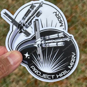 May include: Two stickers with a black and white design. The top sticker has the word "MARY" in white. The bottom sticker has the words "PROJECT HAIL MARY" in white. The stickers feature a spaceship design.