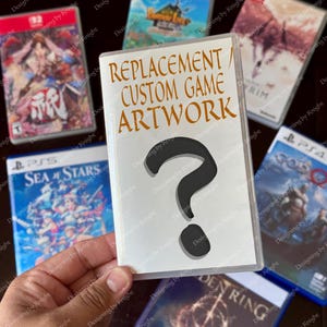 May include: A clear plastic game case with the text "REPLACEMENT / CUSTOM GAME ARTWORK" and a large black question mark. Several video game cases are visible in the background, featuring colorful game art.