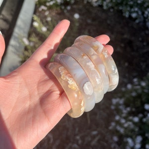 May include: Stack of four agate bangles in shades of white and beige with brown and white patterns. The bangles are smooth and polished.