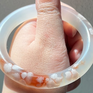 Puede incluir: Pulsera de ágata blanca con un delicado patrón floral y un toque de naranja.