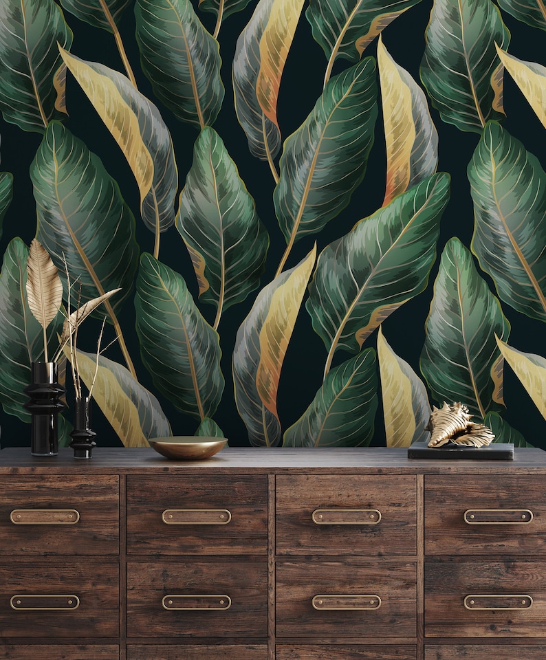 Peut inclure: Une commode en bois fonc&eacute; avec six tiroirs et des poign&eacute;es en laiton. La commode est devant un mur avec un papier peint &agrave; motif de feuilles tropicales dans des tons de vert et d'or.