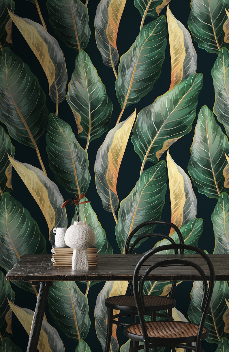 Peut inclure: Un fond bleu fonc&eacute; avec un motif r&eacute;p&eacute;titif de grandes feuilles vertes et dor&eacute;es. Une table en bois avec deux chaises noires se trouve devant le fond &agrave; motifs. Un vase en c&eacute;ramique blanc avec une pile de livres est pos&eacute; sur la table.