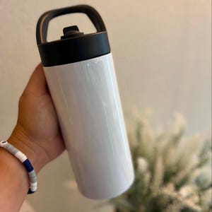 May include: A white cylindrical water bottle with a smooth finish, featuring a black screw-top lid that includes an integrated carrying handle. The bottle has a straight-sided design and a solid white body, providing a clean and simple appearance.
