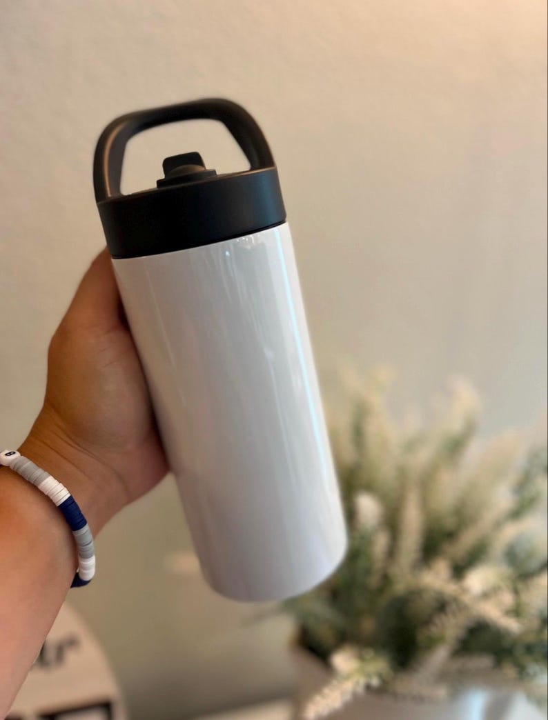 May include: A white cylindrical water bottle with a smooth finish, featuring a black screw-top lid that includes an integrated carrying handle. The bottle has a straight-sided design and a solid white body, providing a clean and simple appearance.