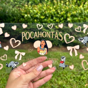 May include: Clear acrylic sign featuring the word "Pocahontas" in gold lettering, with a cartoon image of Pocahontas. The sign includes raccoon illustrations, hearts, and bows. The text "EST. 1995" and "Jamestown Virginia" are also present.