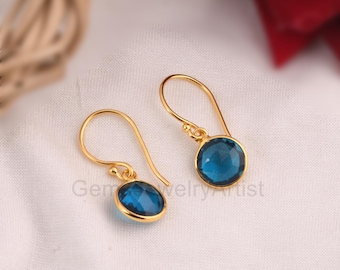 Puede incluir: Un par de pendientes de aro de oro con gotas de piedras preciosas azules. Los pendientes tienen un diseño sencillo y son perfectos para el uso diario.
