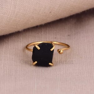 May include: A gold ring with a black gemstone. The ring is adjustable and has a small ball on the end of the band.