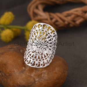 Könnte beinhalten: Ein silberner Ring mit einem filigranen, komplizierten Design. Der Ring ist offen und hat ein breites Band.