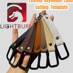 Peut inclure: Plusieurs porte-clés en cuir de différentes couleurs, dont noir, marron et blanc, sont présentés. Chaque porte-clés est doté d'un mousqueton noir et d'un rivet en laiton. Le texte "Leather KeyHolder Laser cutting Template" et le logo Lightburn sont également visibles.