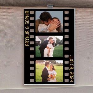 May include: A black film strip-shaped car accessory featuring three wedding photos. The text "ARTHUR & SOPHIA" is printed vertically on the left, and "JUN 08, 2024" is on the right. The accessory is clipped to a car visor.