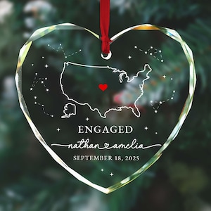 May include: Heart-shaped clear glass ornament with a red ribbon. The ornament displays a map of the United States, constellations, and the words "ENGAGED" and the names "nathan & amelia" with the date "SEPTEMBER 18, 2025".