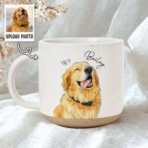 May include: A cream-coloured ceramic mug featuring a Golden Retriever dog illustration, with the name "Bailey" written above. The mug has a brown base and a white handle. The words "UPLOAD PHOTO" are visible.