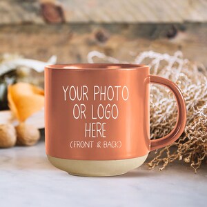 Op de afbeelding: Een terracottakleurige keramische mok met een witte handgreep. De mok heeft een witte inscriptie met de tekst "Uw foto of logo hier (voor- en achterkant)".