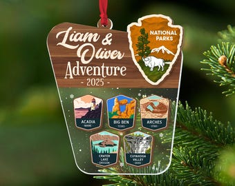 Puede incluir: Un adorno de madera con el texto Liam & Oliver Adventure 2025, un logotipo de punta de flecha de National Parks con un bisonte y cinco iconos hexagonales más pequeños que representan los parques nacionales Acadia, Big Ben, Arches, Crater Lake y Cuyahoga Valley.