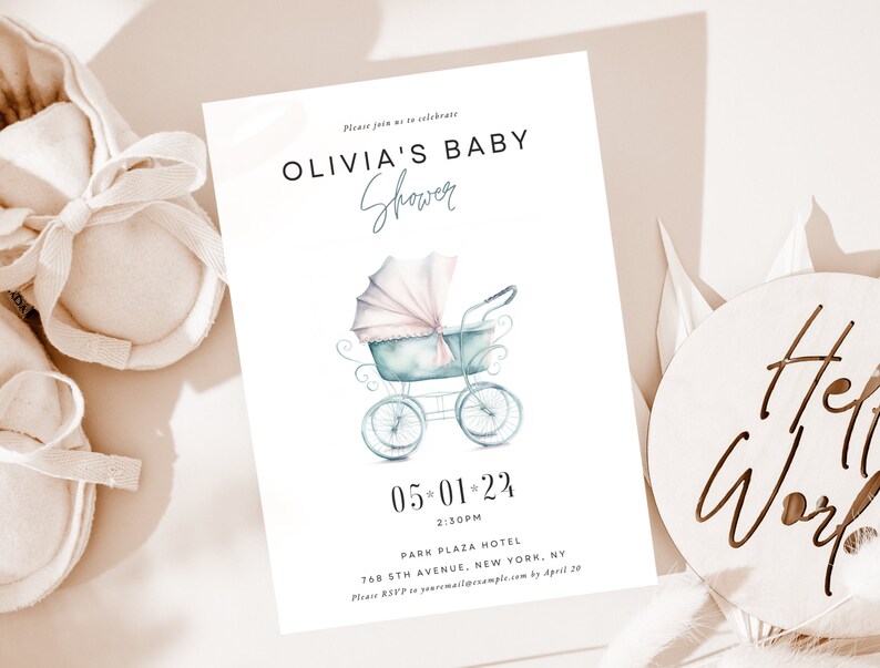Op de afbeelding: Een uitnodiging voor een babyshower met een aquarel illustratie van een vintage kinderwagen in pastelblauw en roze. De uitnodiging bevat de tekst "OLIVIA'S BABY Shower" en evenementdetails. Zachte babyschoentjes en een houten bord met "Hello World" staan op de achtergrond.