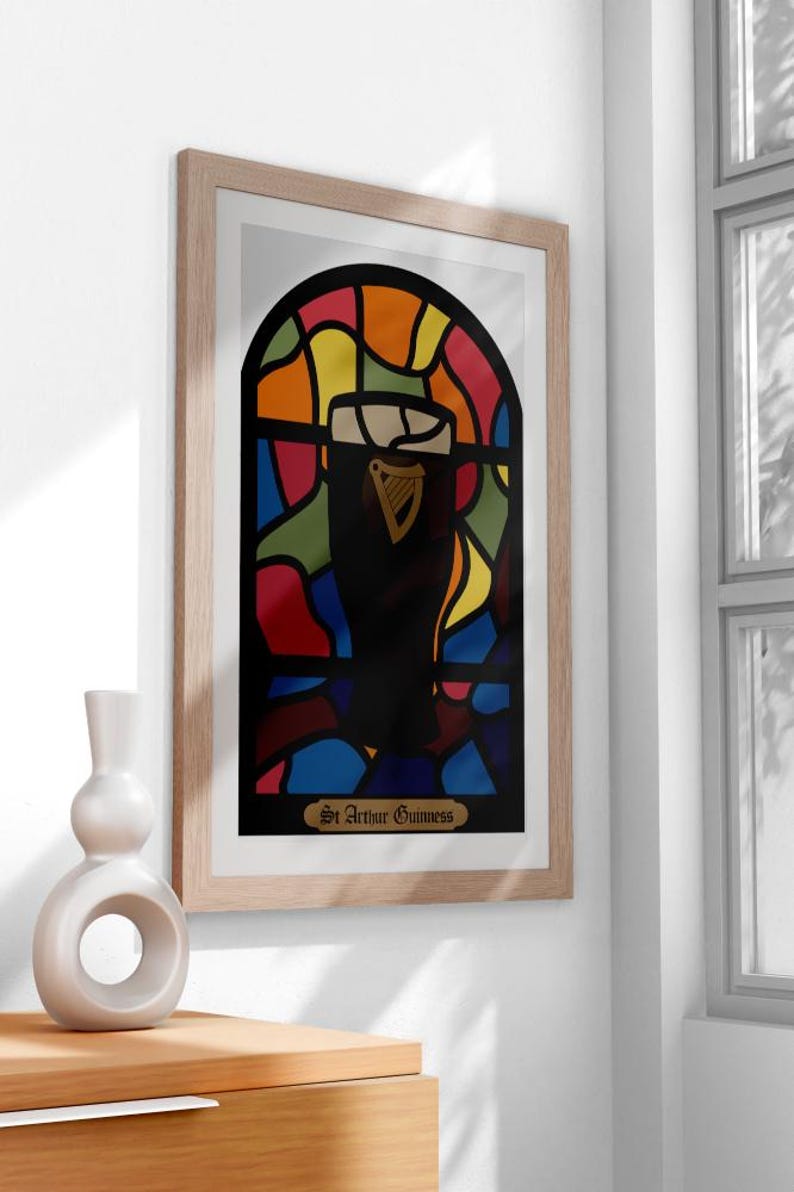 May include: A framed print of a stained glass window design featuring a glass of Guinness beer. The window is made up of colorful pieces of glass in shades of red, orange, yellow, green, blue, and purple. The text at the bottom of the print reads "St. Arthur Guinness."