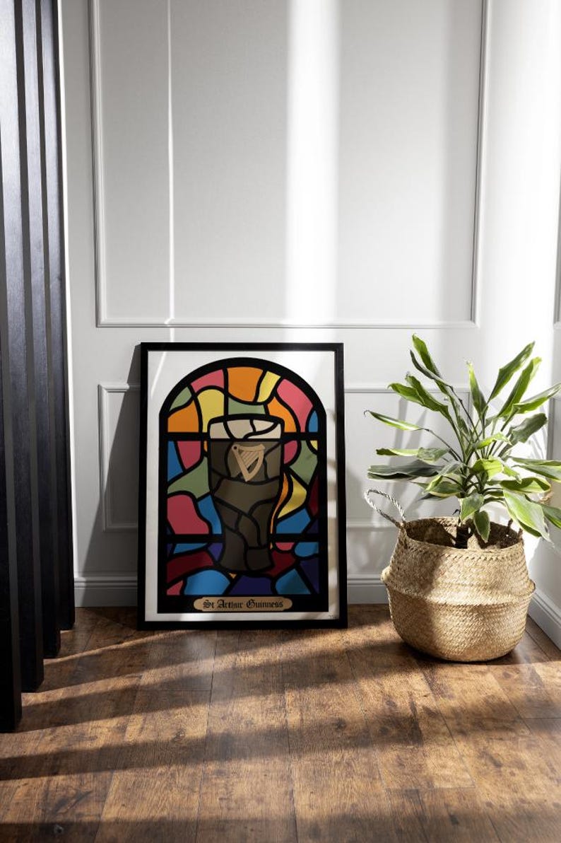 May include: A framed print of a stained glass window design featuring a glass of Guinness beer. The window is made up of colorful pieces of glass in shades of red, orange, yellow, green, blue, and purple. The text at the bottom of the print reads "Sir Arthur Guinness".
