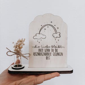 Könnte beinhalten: Ein dekoratives Holzstück mit einem Regenbogen und deutschem Text. Es enthält ein kleines Glasfläschchen mit Trockenblumen, die mit Bindfaden gebunden sind. Der Text lautet "die liebe bleibt, auch wenn du die regenbogenbrücke gegangen bist."