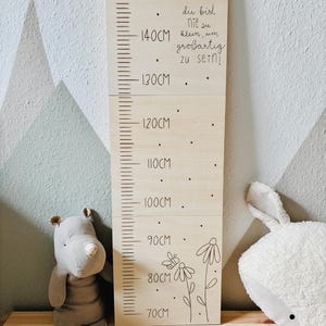 May include: A wooden height chart with measurements up to 150cm. The chart has a decorative top edge and features a floral design with a butterfly. Text on the chart reads "du bist nie zu klein, um großartig zu sein!"