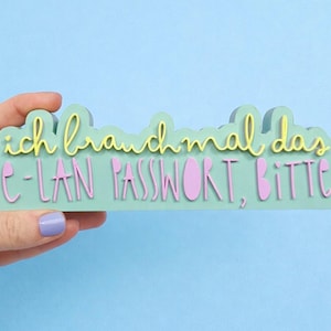 Può includere: Un cartello verde menta con la frase tedesca "ich brauch mal das C-LAN PASSWORT, BITTE" in lettere gialle e rosa. Il cartello ha una forma a nuvola ed è tenuto su uno sfondo blu.