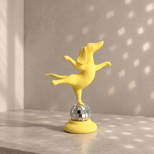 Könnte beinhalten: Eine leuchtend gelbe Hundefigur in dynamischer Pose, die auf einem Bein auf einer kugelförmigen Discokugel balanciert. Die Discokugel hat eine reflektierende, verspiegelte Oberfläche aus kleinen quadratischen Plättchen.