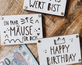 May include: Three white wooden gift card holders with black lettering and decorative cutouts. One says "WEIL DU ES WERT BIST", another "EIN PAAR MÄUSE FÜR DICH", and the third "HAPPY BIRTHDAY". Euro banknotes are visible.