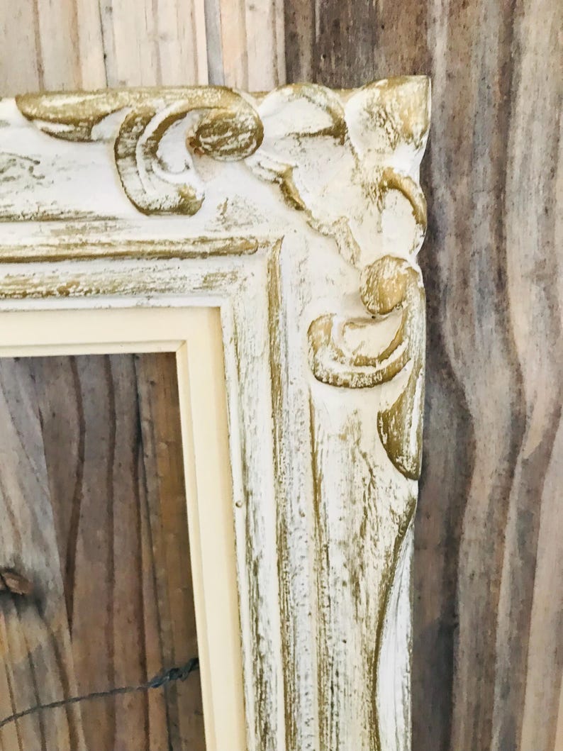 May include: A rectangular picture frame featuring an ornate, raised relief pattern along the edges. The frame has a distressed finish with a base of off-white paint accented by gold-toned highlights on the decorative scrollwork and corner details.