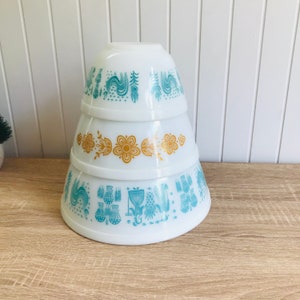 以下が含まれることがあります： 青と金の色の花柄が施された白い入れ子状のボウル4個セット。ボウルはピラミッド型に積み重ねられています。