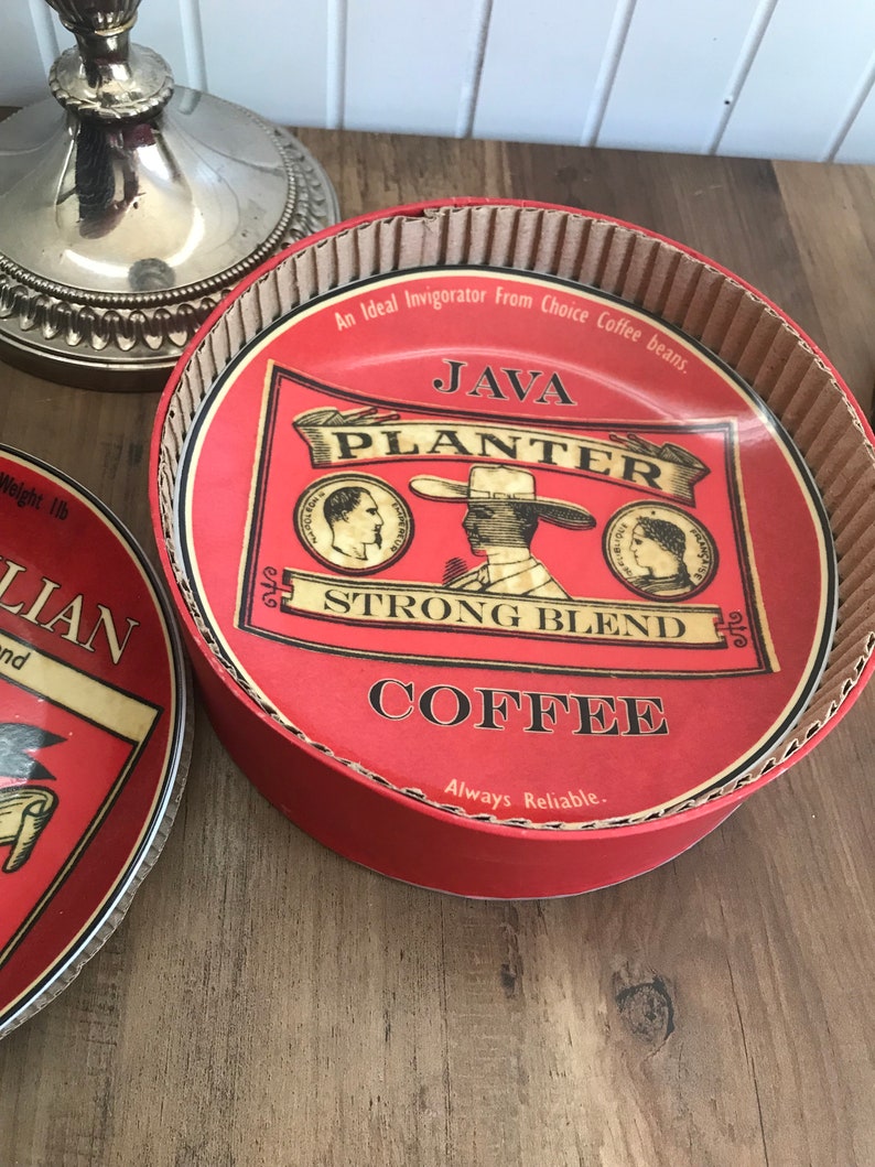 May include: A red and white cardboard box with a red lid. The lid has a vintage coffee advertisement for Java Planter Strong Blend Coffee. The text on the lid reads "An Ideal Invigorator From Choice Coffee Beans. Java Planter Strong Blend Coffee. Always Reliable."