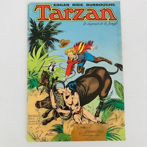 Könnte beinhalten: Ein Vintage-Comic-Cover mit Tarzan, dem Herrn des Dschungels, der mit einem Stier ringt. Das Cover ist in französischer Sprache und trägt den Titel "Tarzan" in roten Buchstaben. Der Comic stammt aus der Edgar Rice Burroughs-Reihe.
