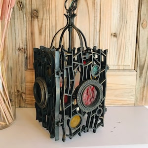 Könnte beinhalten: Eine dunkle Metall-Hängelaterne mit geometrischem Design. Die Laterne verfügt über kreisförmige Buntglasakzente in Rot, Gelb und Grün. Die Laterne ist an einer Kette aufgehängt und hat eine dekorative Oberseite.