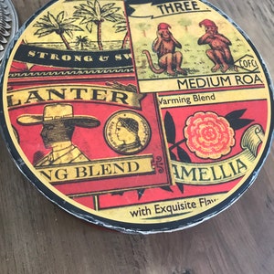 May include: A round, red, yellow, and black tin container with the text "PALMS BRAND THREE" and "MEDIUM ROA Varming Blend" on the front. The tin also features images of monkeys, palm trees, and a woman's face.