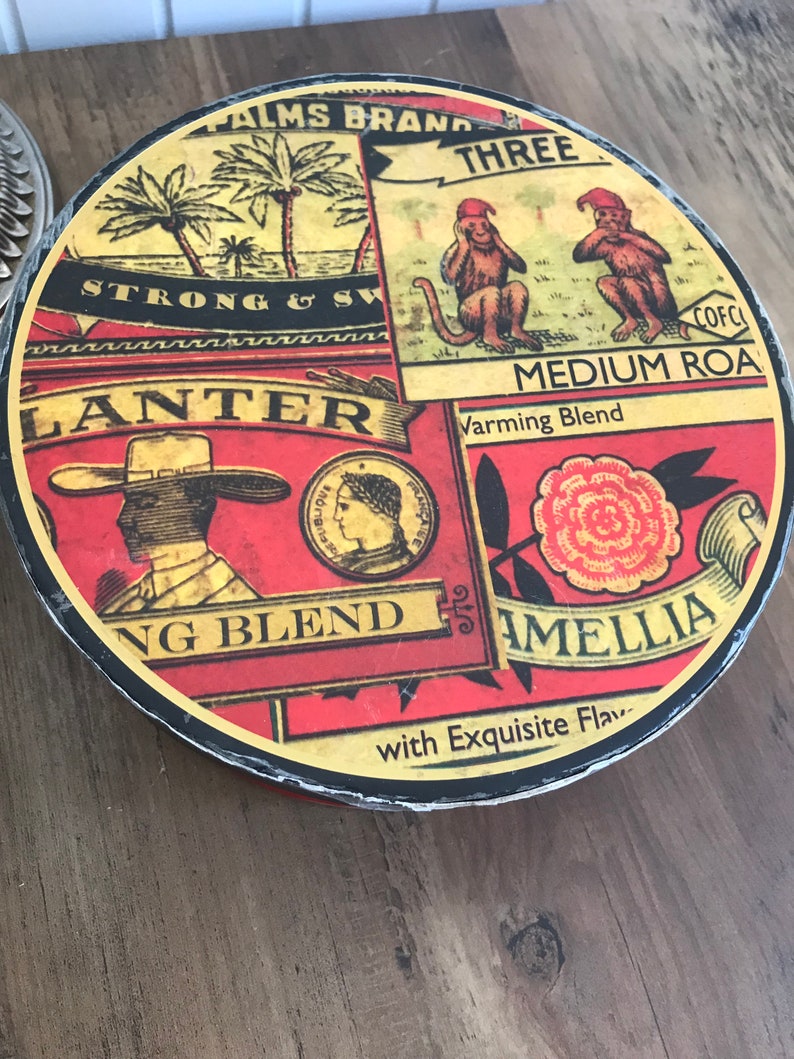 May include: A round, red, yellow, and black tin container with the text "PALMS BRAND THREE" and "MEDIUM ROA Varming Blend" on the front. The tin also features images of monkeys, palm trees, and a woman's face.